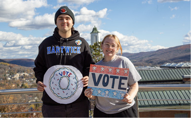 Two Oneonta residents holding handmade voting signs overlooking the city